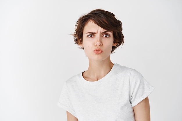 Skeptical caucasian woman look perplexed , pucker lips and raising eyebrow suspicious, feeling doubtful or unsure, standing on white wall