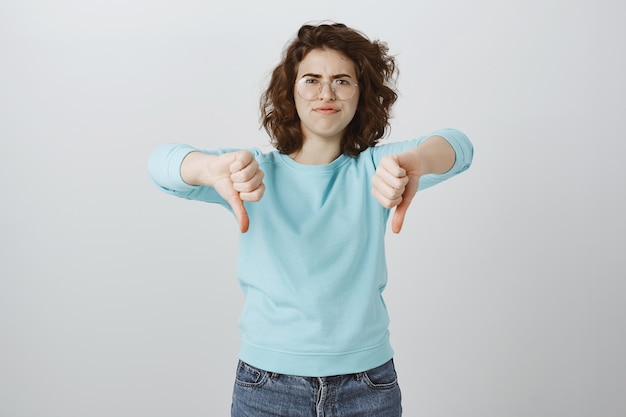 Skeptical and disappointed woman showing thumbs-down, very bad, awful result, exress dislike