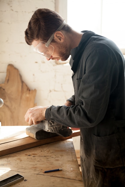 Free photo skilled young carpenter doing woodwork, working with electric sander, vertical