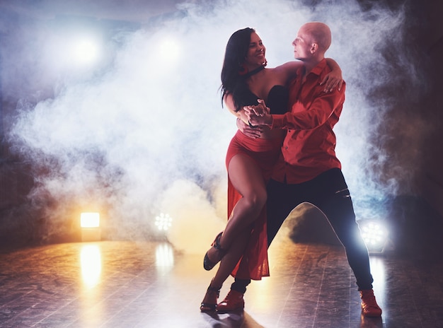 Free photo skillful dancers performing in the dark room under the concert light and smoke. sensual couple performing an artistic and emotional contemporary dance