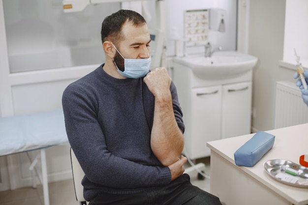 Free photo skillful nurse is doing blood test for man in clinic. man in a medical mask.