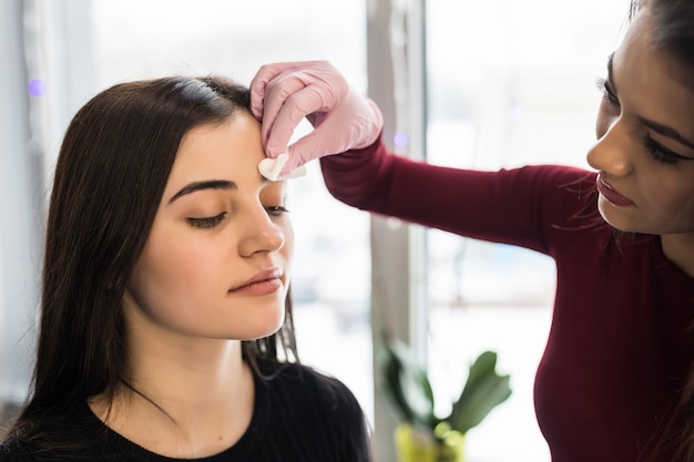 Skillful visagiste doing black eyebrows make-up for a young woman