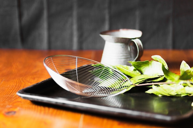 Skimmer and jug with leaves in black tray over the table