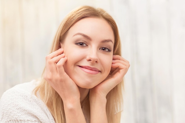 Free photo skincare concept. pretty blond lady in white dress sitting with her hands on the cheeks isolated on white.