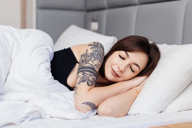 Sleeping brunette woman lie on the bed in the morning wake up stretching her arms and body