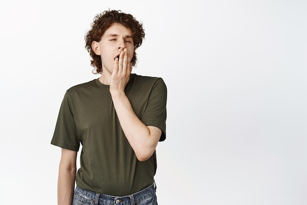 Free Photo sleepy male student with curly hair yawning with tired face yawn from boredom standing in tshirt over white background