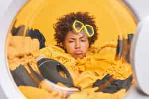 Free photo sleepy tired curly haired woman housewife looks overworked washing buried in laundry