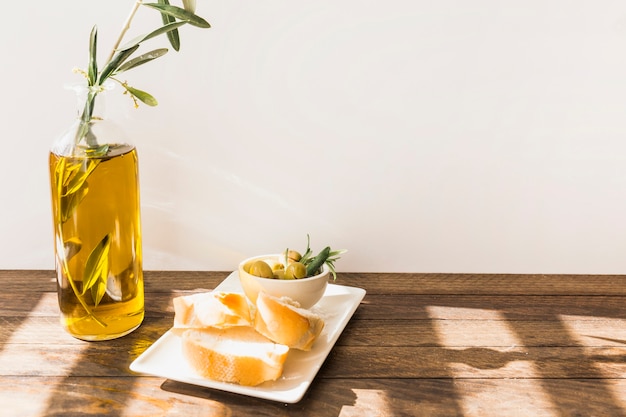 Slice of bread with bowl of olives on wooden table