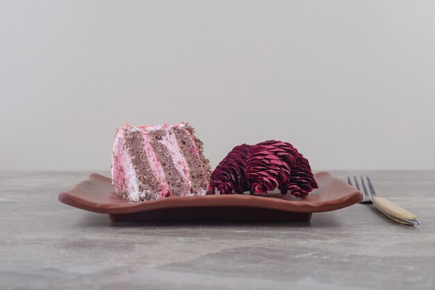 A slice of cake and red pine cones on a platter next to a fork on marble 