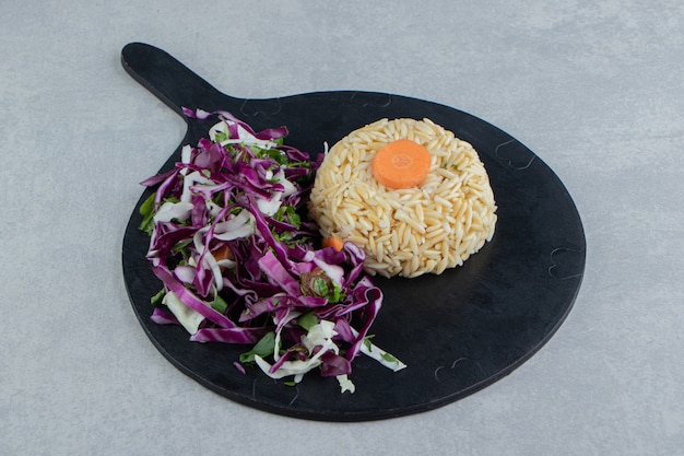 Free photo a slice of carrot on the rice next to salad, on the board , on the marble background.