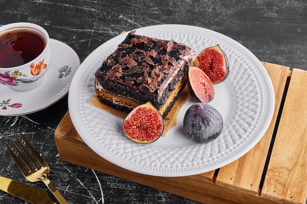 A slice of chocolate cake with fruits and a cup of tea in a white plate. 