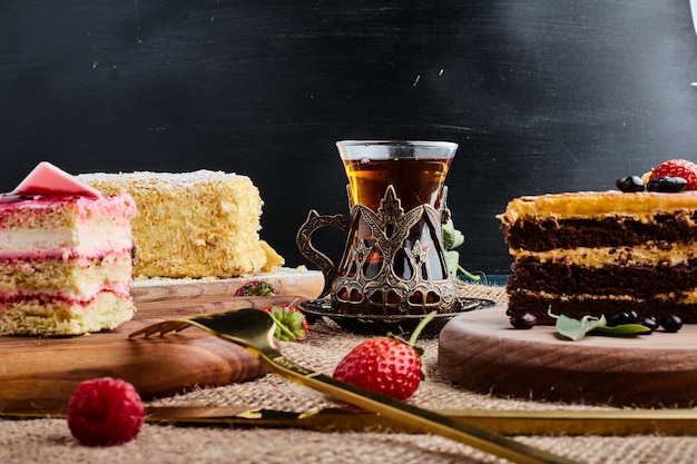 A slice of chocolate cake on a wooden board with a glass of tea. 