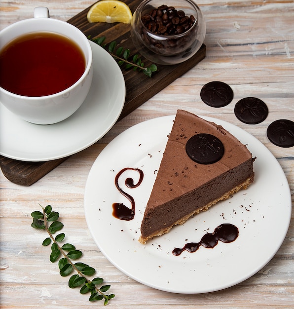 A slice of chocolate mousse cheesecake with chocolate chips and a cup of tea. 