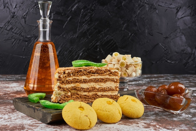 A slice of honey cake with butter cookies and a bottle of drink. 