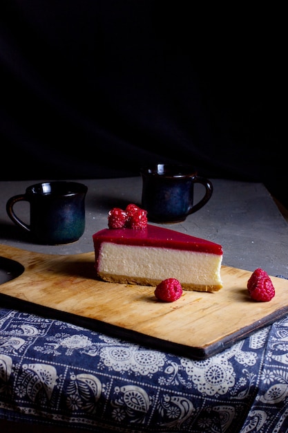 A slice of raspberry cheesecake placed on wooden cutting board