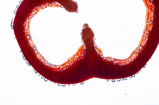 Slice of red pepper floats in water on white background