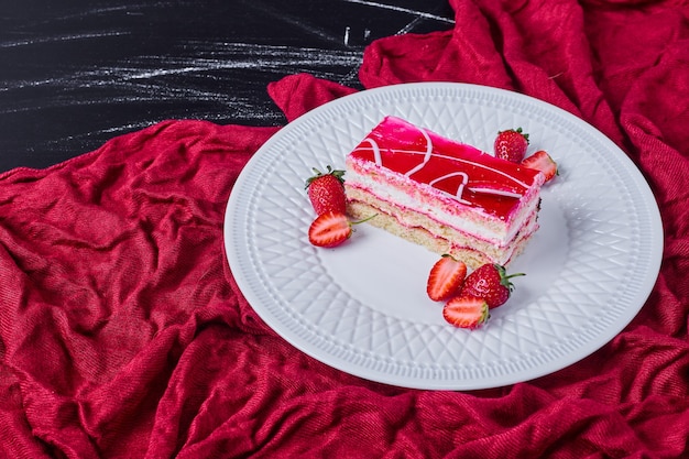 Free photo a slice of strawberry cake on a white plate on dark background.