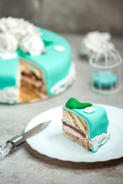 Slice of a turquoise cake decorated with white roses and green leaves