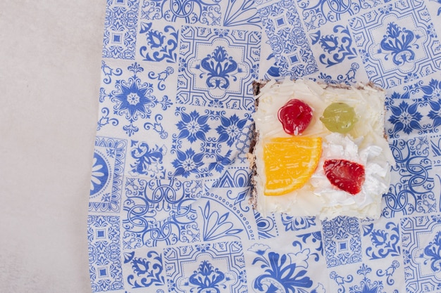 Free photo slice of white cake with fruit slices on tablecloth.