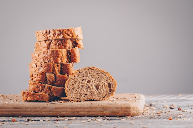 Free photo sliced bread in a cutting board side view on a wooden table and gray surface