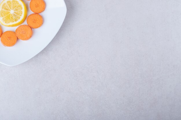 Sliced carrot and lemon on a plate on marble table.