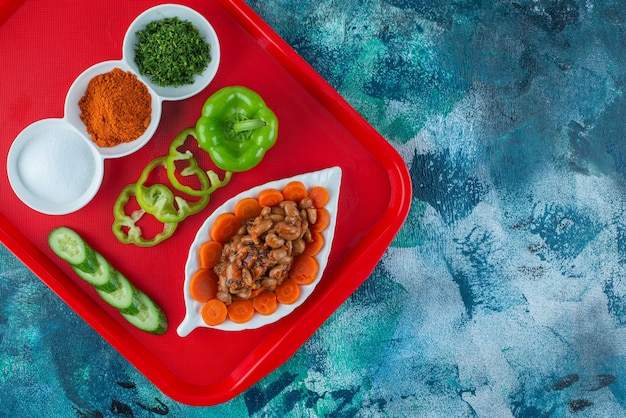 Free photo sliced carrots and beans and vegetables on a plate on a tray, on the blue table.