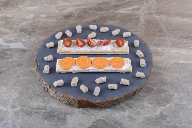 Sliced carrots, and tomatoes on crispbreads, surrounded by crumb on the board, on the marble surface