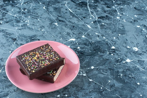 Sliced chocolate coated waffle on a plate, on the blue table. 