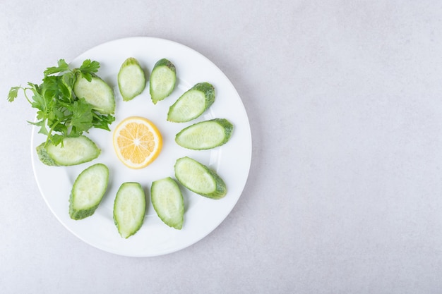 Sliced cucumber, lemon and parsley on a plate, on the marble.