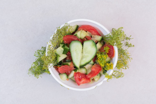 Sliced cucumbers and tomatoes in white bowl with greens