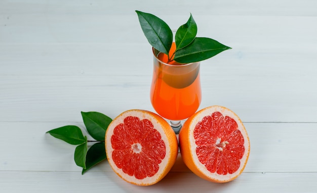 Free photo sliced grapefruit with leaves and juice on wooden surface, flat lay.