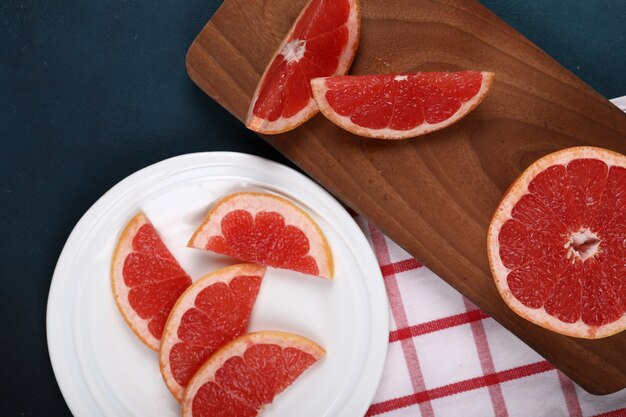 Sliced grapefruits in a white plate and on a wooden board.