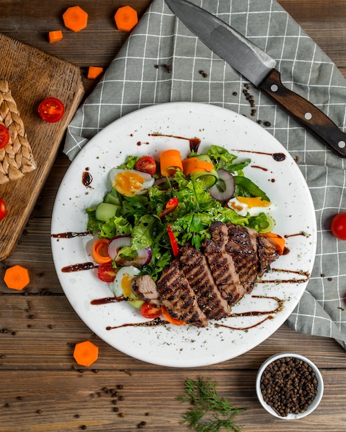 Free photo sliced grilled beef steak served with green salad with eggs