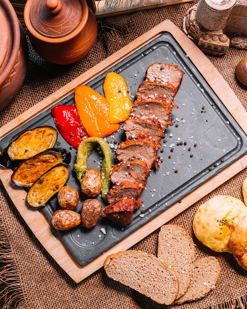 Free photo sliced grilled steak on the wooden board eggplant potato bel pepper top view