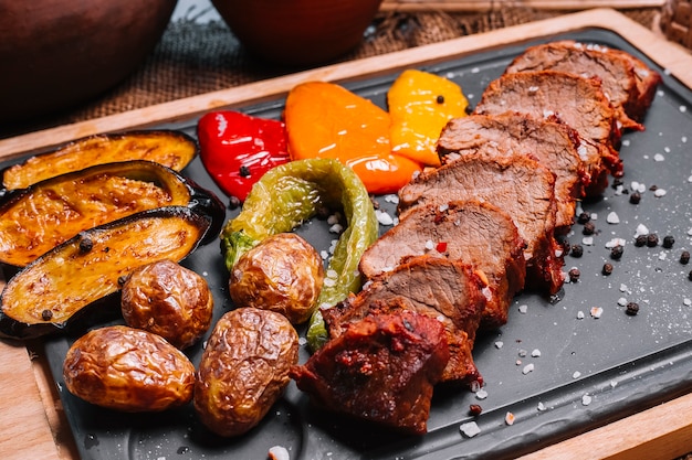 Sliced grilled steak on the wooden board eggplant potato bell pepper side view