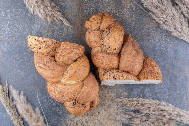 Sliced halves of strucia bread and bundle of wheat stalks on marble surface