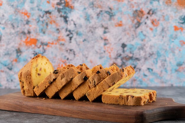 Sliced homemade roulette cake on wooden chopping board over grey table. 