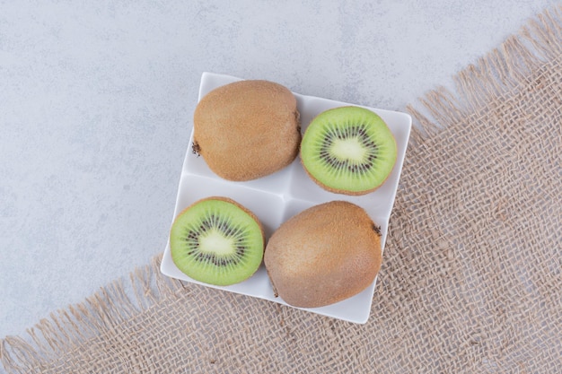 Free photo a sliced kiwi in white plate on sackcloth . high quality photo