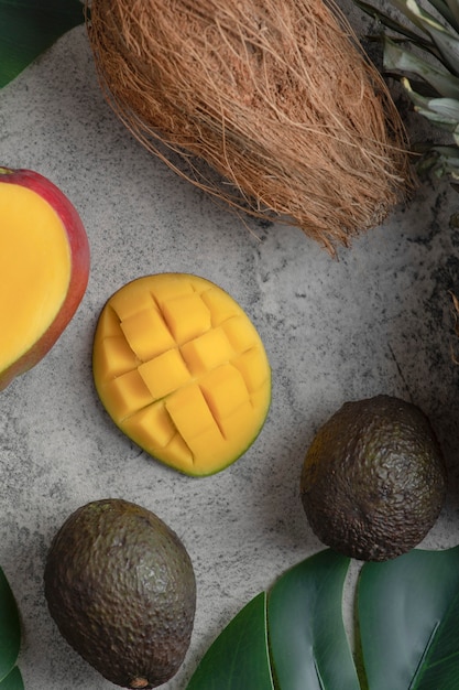 Free photo sliced mango, coconut and ripe avocado fruits on marble surface.