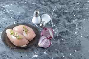 Free photo sliced onion and chicken breast on a plate , on the marble background.