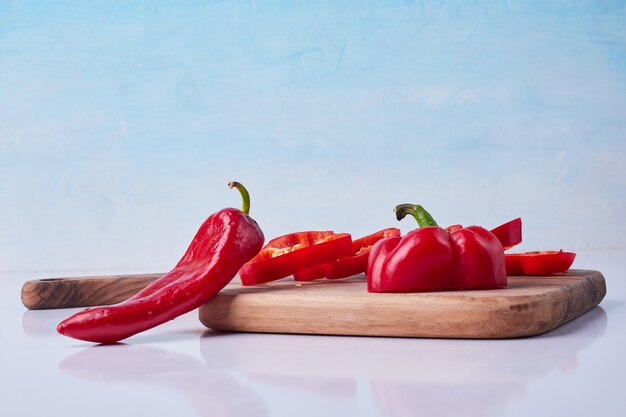 Sliced red chili and bell peppers on a wooden platter on blue.