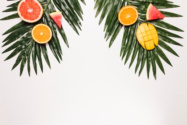 Free photo sliced ripe red watermelon orange mango at palm leaf