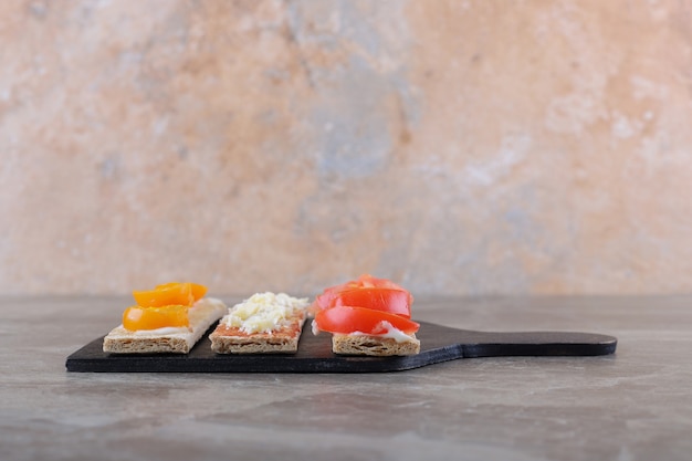 Sliced ripe and unripe tomatoes on crispy breads on the cutting board, on the marble surface