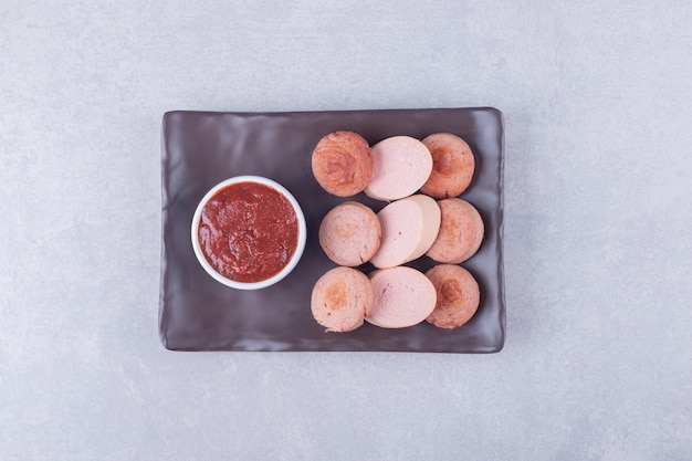 Sliced sausages with ketchup on dark plate. 