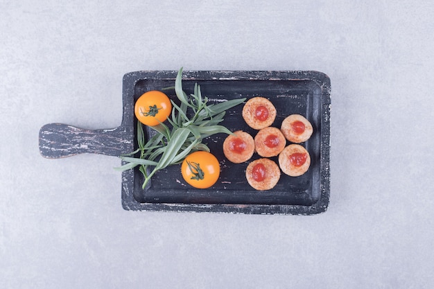 Sliced sausages with ketchup and tomatoes on black board. 