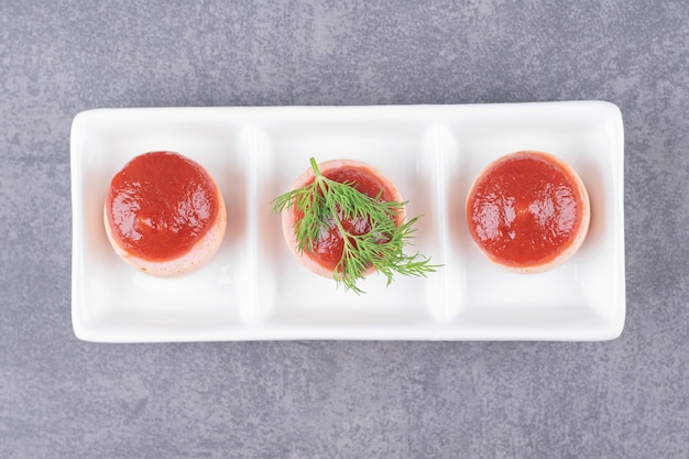 Sliced sausages with ketchup on white plate. 