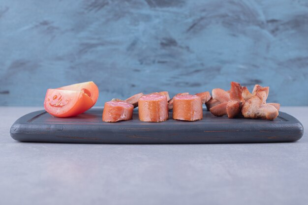 Sliced sausages with tomatoes on dark board.