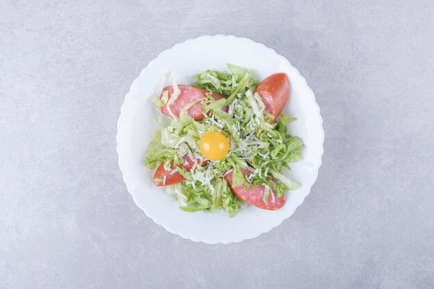 Sliced smoked sausages, lettuce and egg yolk in white bowl. 