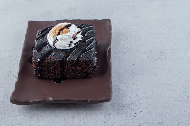 Sliced of tasty chocolate brownie with cream on dark plate. High quality photo