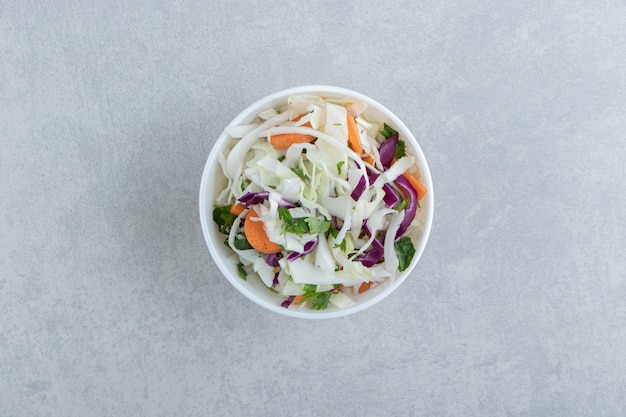 Sliced tomato, greens, red cabbage in bowl , on the marble background.